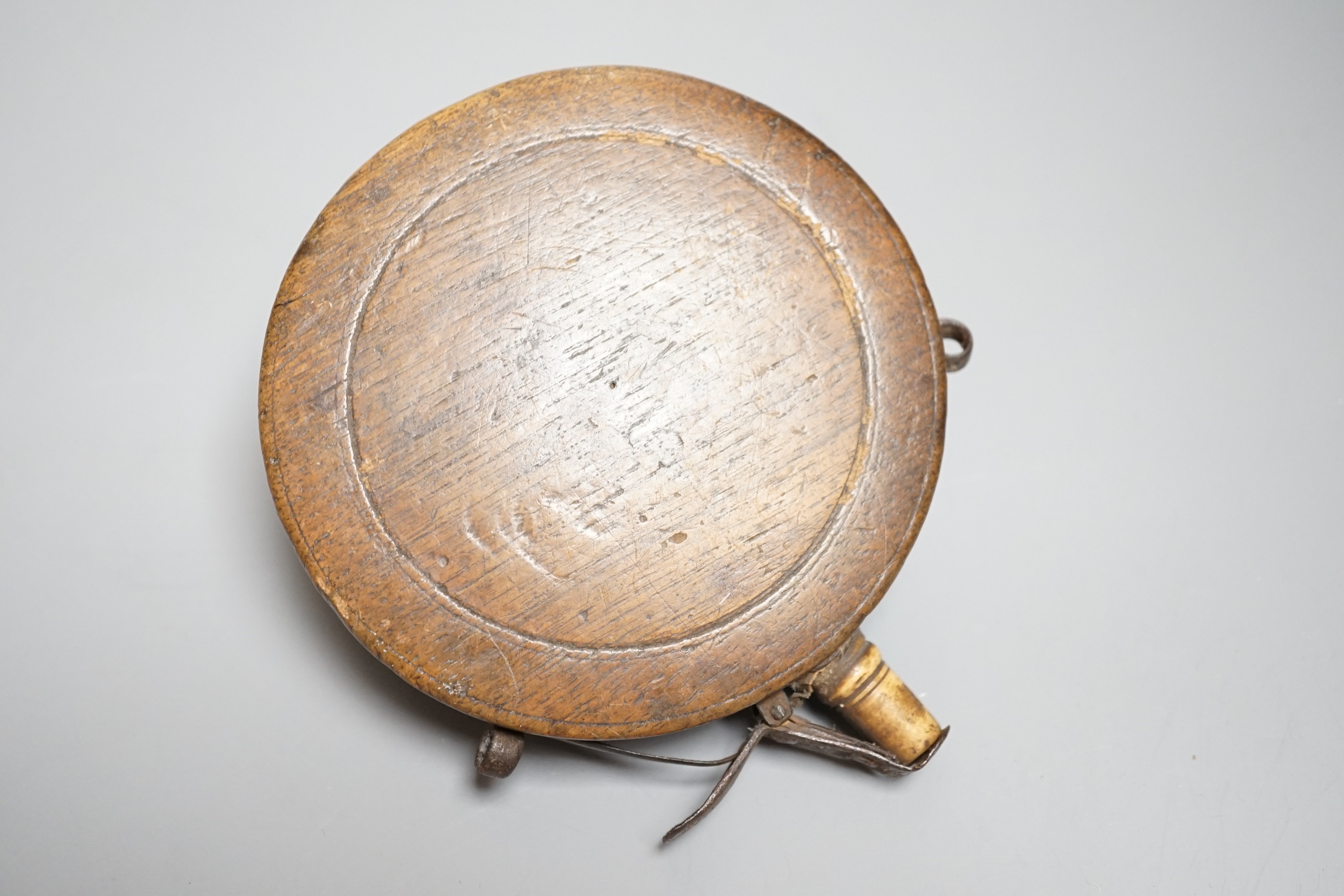 A circular wooden powder flask 17th century, carved with bear, hound and fox, and lion’s mask in low relief surrounded by game counter, engraved brass border, iron lever charger, turned bone nozzle. Diameter 11cms